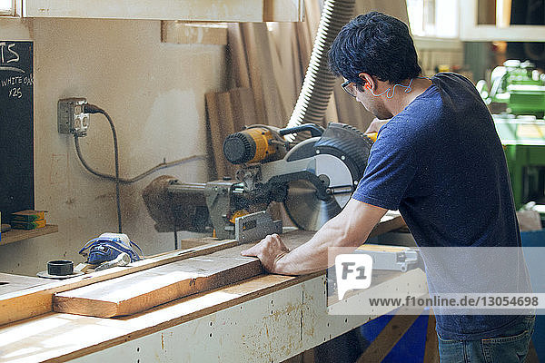 Seitenansicht eines männlichen Zimmermanns beim Schneiden von Holzbrettern mit der Elektrosäge