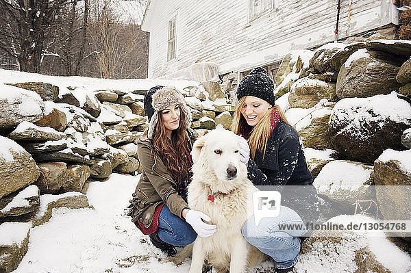 Glückliche Freundinnen mit Hund bei Steinen im Winter