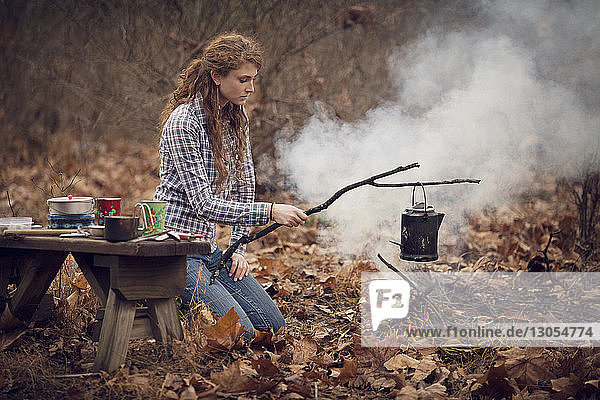 Frau macht Getränk am Lagerfeuer im Wald