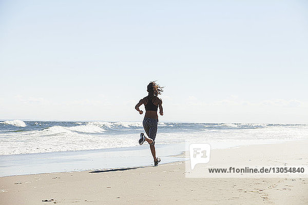 Rückansicht einer Frau  die an einem sonnigen Tag am Strand läuft
