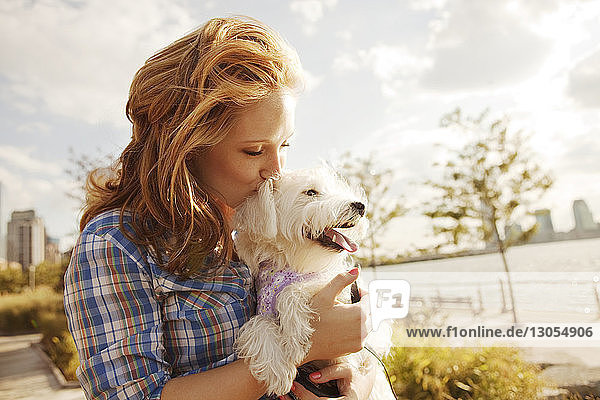 Woman kissing dog against sky on sunny day