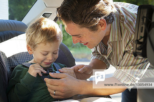 Happy father assisting son in fastening seat belt