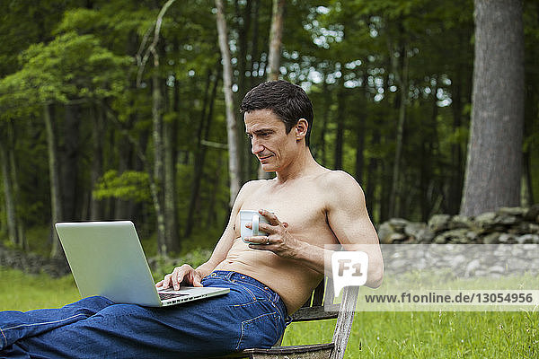 Mann mit Kaffeetasse mit Laptop-Computer  während er auf einem Stuhl im Feld sitzt