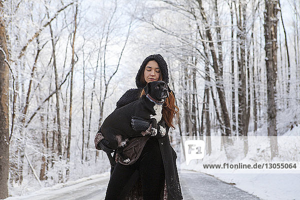 Woman carrying dog while standing on road during winter