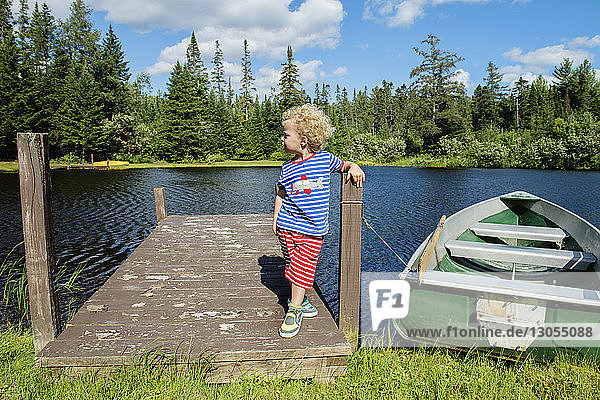 Boy standing on jetty by moored boat at lakeshore