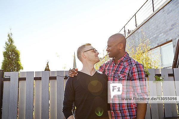 Happy man arm around with boyfriend while looking at him on sunny day