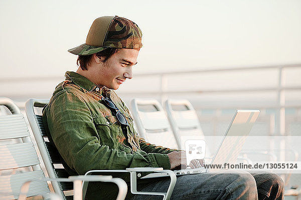 Mann benutzt Laptop-Computer  während er auf einem Liegestuhl im Schiff sitzt