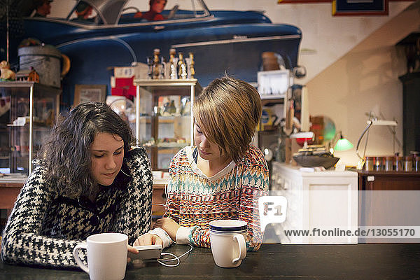 Freunde benutzen Mobiltelefon  während sie im Café sitzen