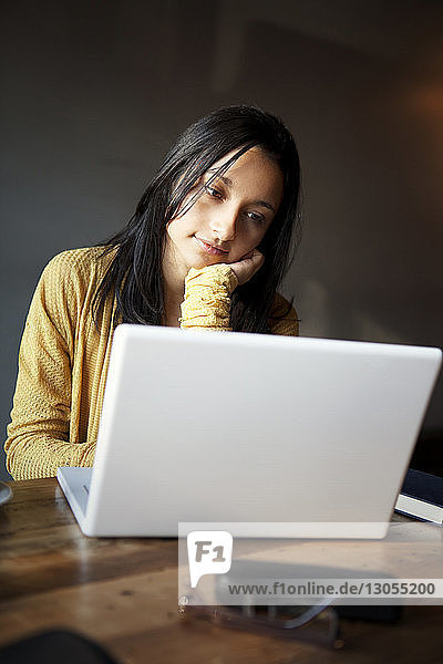 Nachdenkliche Frau benutzt Laptop  während sie im Haus am Tisch sitzt