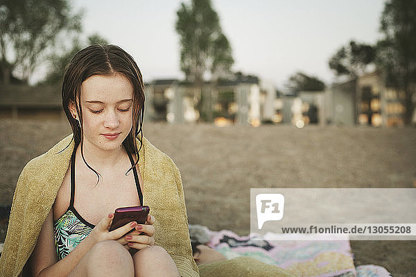 Mädchen benutzt Mobiltelefon  während sie am Strand sitzt