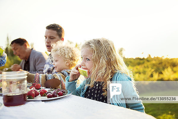 Girl eating watermelon with family on picnic table
