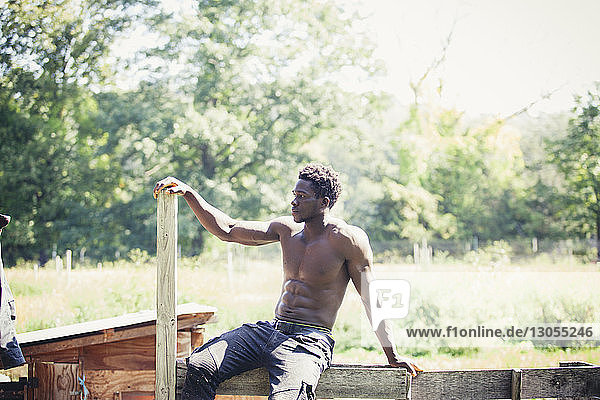 Thoughtful muscular man sitting on wood during sunny day