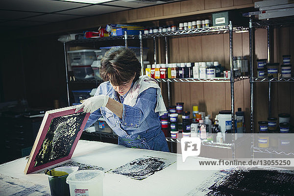Handwerkerin untersucht Tintendrucke auf der Werkbank in einem Workshop
