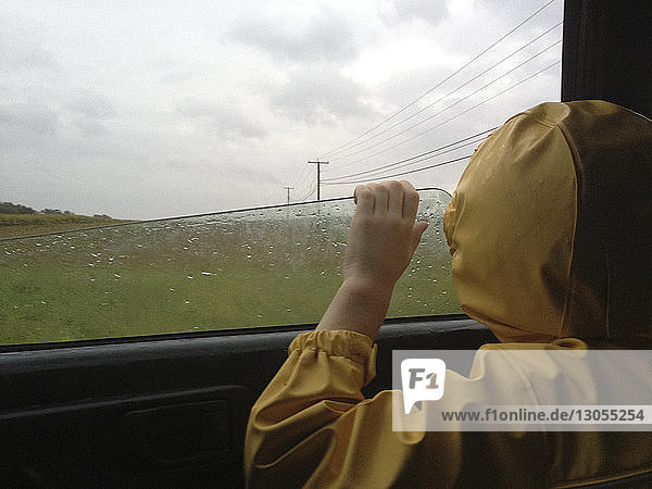 Rückansicht eines Jungen  der während der Regenzeit durch ein Autofenster schaut