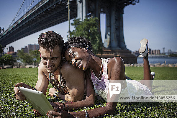 Glückliches Paar mit Tablet-Computer auf dem Feld liegend mit Manhattan Bridge im Hintergrund