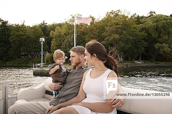 Mann trägt Sohn  während er mit Frau im Boot auf dem See Arm in Arm sitzt