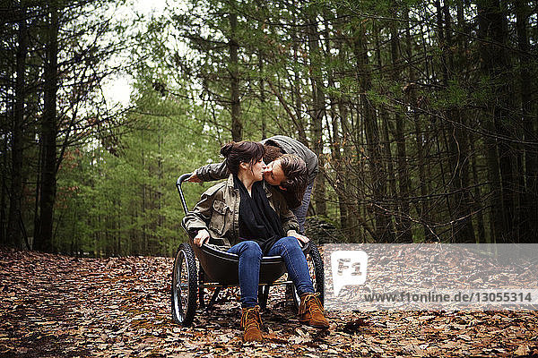 Man kissing woman sitting on wheelbarrow