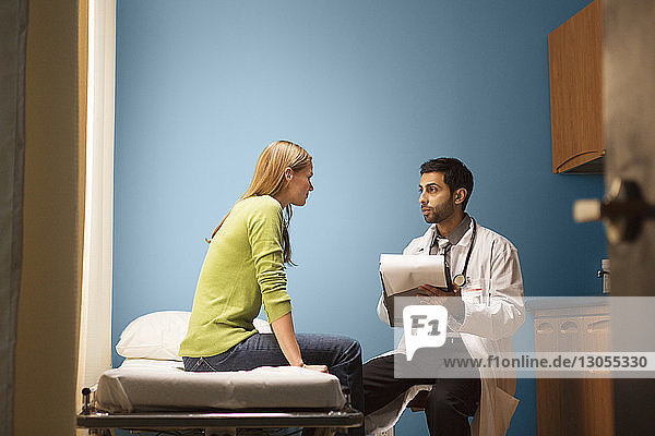 Doctor holding file while looking at patient in hospital