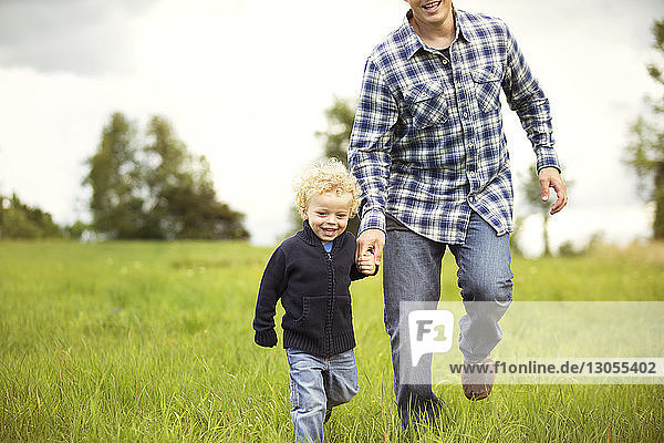 Happy father and son walking on grassy field
