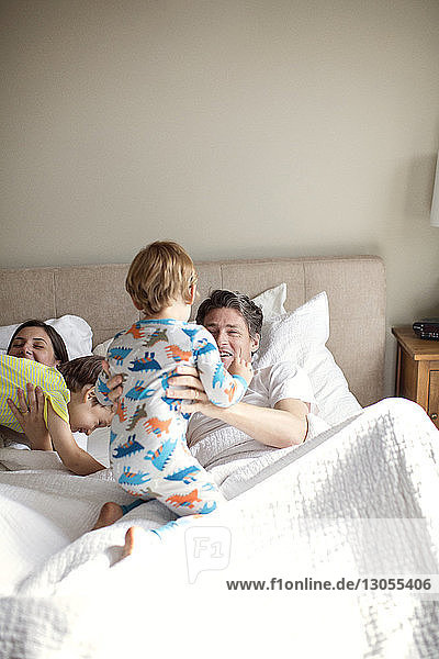 Happy parents playing with sons while lying on bed