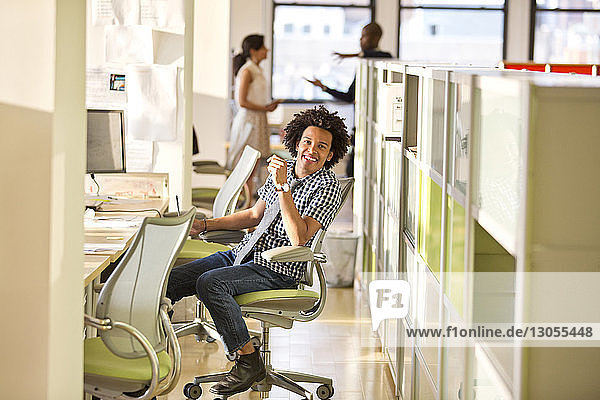 Porträt eines glücklichen Geschäftsmannes  der auf einem Stuhl im Büro sitzt