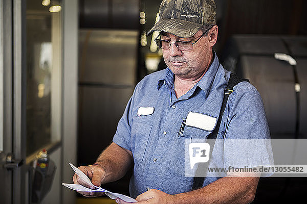 Serious worker examining documents while standing in metal industry