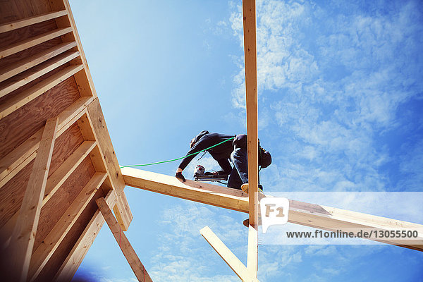 Niedrig-Winkel-Ansicht eines Arbeiters  der Konstruktionsrahmen gegen blauen Himmel herstellt