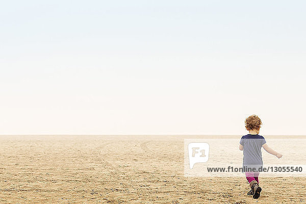 Rear view of girl walking on sand at beach