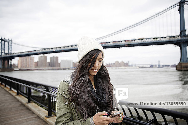 Frau telefoniert  während sie auf der Promenade gegen die Manhattan-Brücke in der Stadt steht