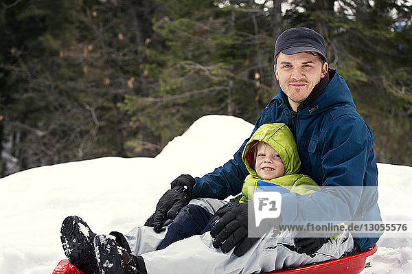 Portrait of father sitting with son on sled