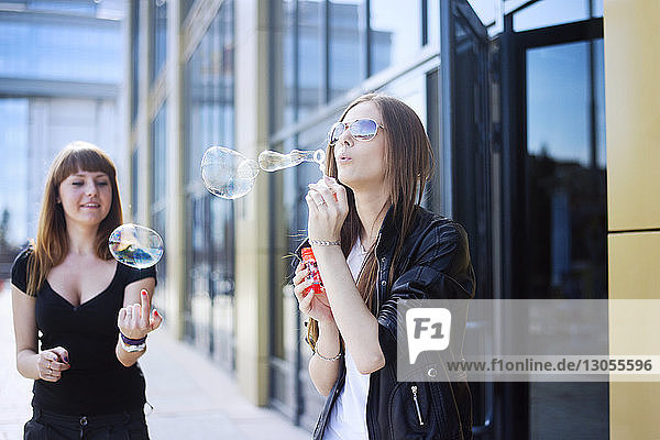 Woman blowing soap bubbles while friend playing in city