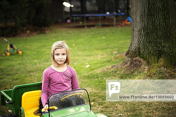 Porträt eines selbstbewussten Mädchens  das im Spielzeugauto im Hinterhof sitzt