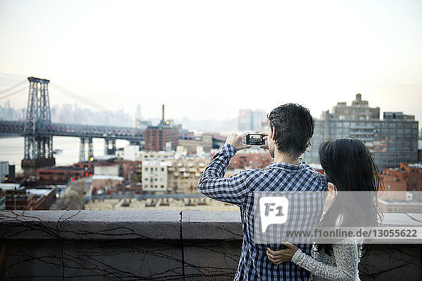 Rear view of couple photographing cityscape against sky