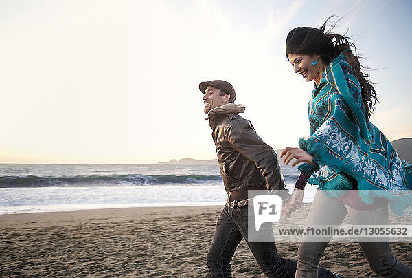 Glückliches junges Paar hält sich an den Händen und geht am Strand