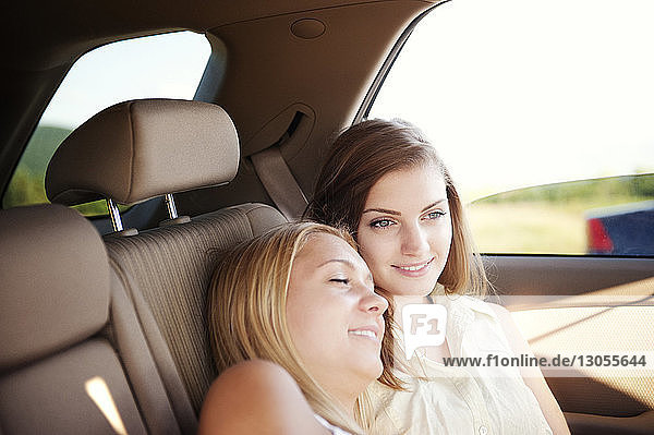 Lächelnde Frau entspannt sich auf der Schulter eines Freundes  während sie im Auto sitzt