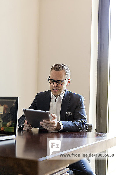Geschäftsmann benutzt Tablet-Computer  während er im Büro am Tisch sitzt