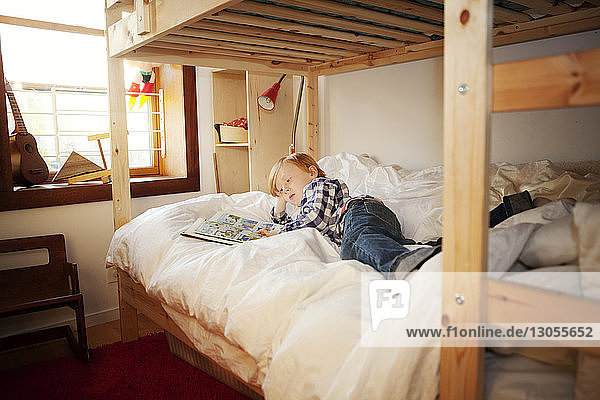 Boy looking book while lying on bunked at home