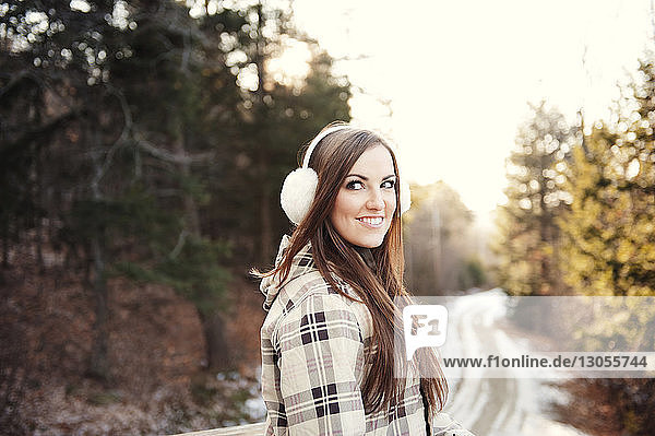 Glückliche Frau trägt Ohrenschützer  wenn sie im Winter auf einem Gehweg steht