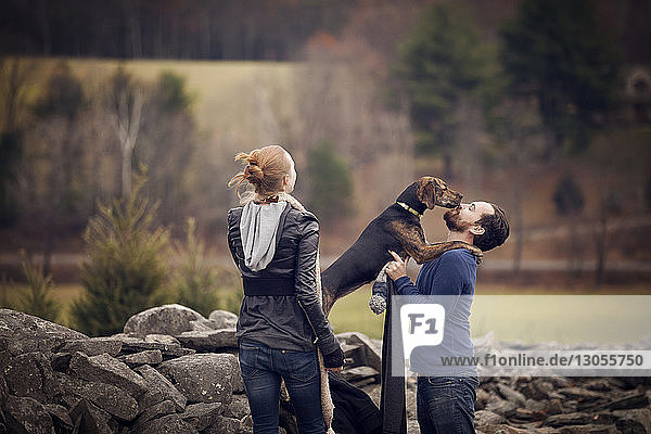 Woman looking man playing with dog by stone wall