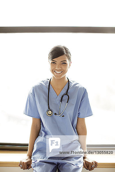 Porträt einer lächelnden Ärztin auf dem Fensterbrett sitzend