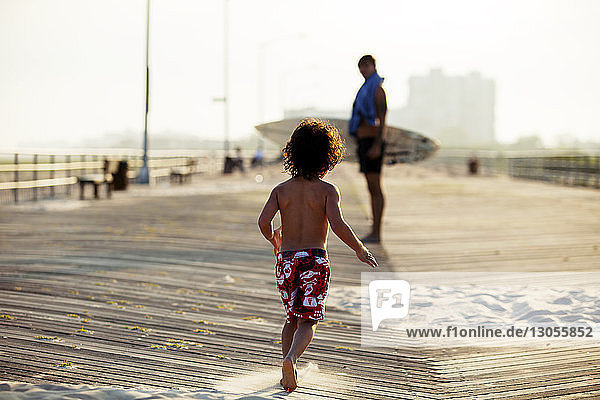 Rückansicht eines Jungen  der bei Sonnenuntergang auf dem Pier läuft