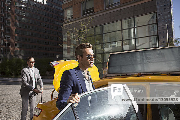 Geschäftsmann steigt mit einem Kollegen im Hintergrund in ein Taxi