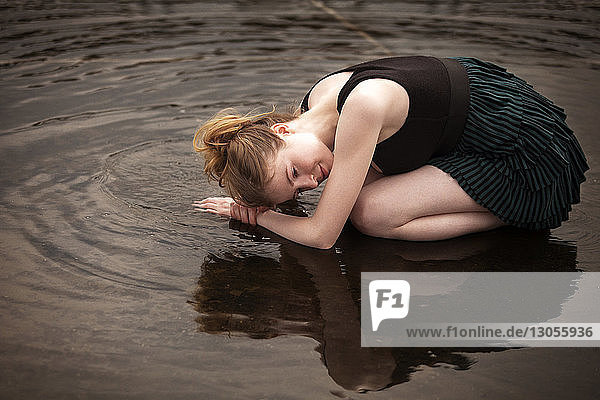 Side view of woman kneeling on shallow water at beach