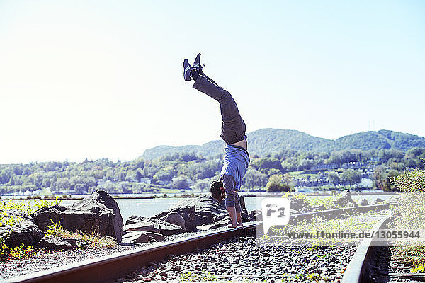 Seitenansicht eines Mannes beim Handstand auf einem Eisenbahngleis am Fluss