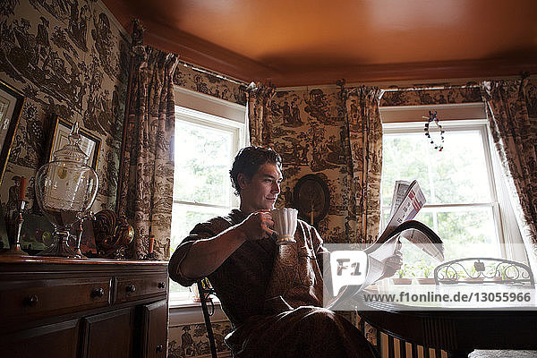 Mann liest Zeitung  während er zu Hause eine Teetasse hält