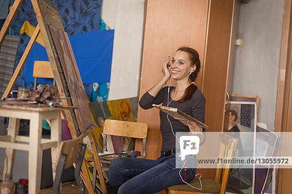 Glückliche Frau hört Musik beim Malen im Kunstunterricht