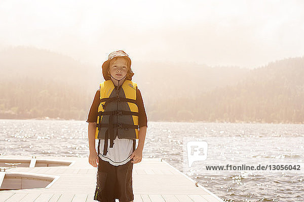 Porträt eines Jungen in Rettungsschwimmerjacke  der am Pier gegen den Himmel steht