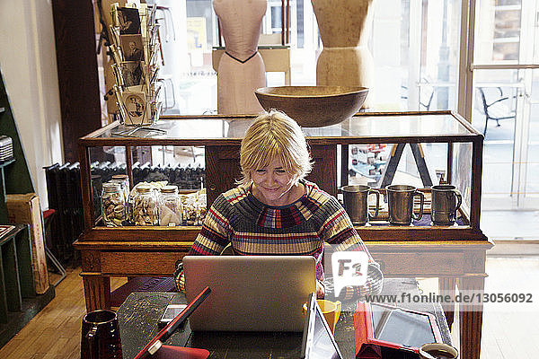 Happy woman using laptop computer while sitting at clothing store