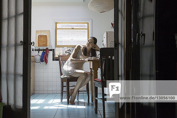 Schwangere Frau schaut weg  während sie auf einem Stuhl in der Küche sitzt