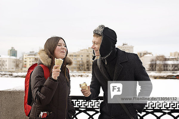 Happy couple eating ice cream during winter at park